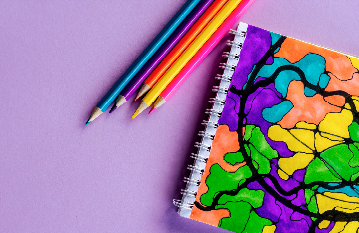 An example of colorful neurographic art drawn in a notebook, with colored pencils sitting next to it, on a lavender background.